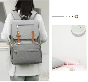 Detail of light grey diaper bag showing side USB charging port and brown leather straps