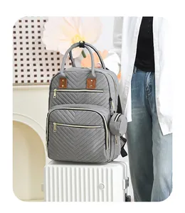 Close-up of gray quilted diaper bag with gold zippers on a white striped suitcase