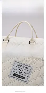 Detail of cream quilted travel bag showing reinforced carry handles and fashion patch