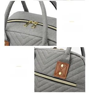 Detail of grey quilted mommy bag with golden zippers and brown leather handle patches
