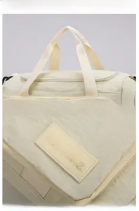 Detailed macro view of the cream travel bag featuring wide straps and brand logo patch