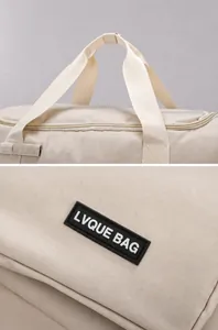 Détails des poignées renforcées et du logo en caoutchouc sur le sac de voyage crème