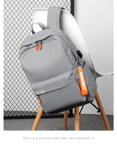 Detail view of grey backpack showing USB charging port and orange zipper accents