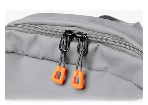 Close-up of durable two-way zippers with orange ergonomic pullers on grey backpack