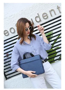 Slim blue laptop sleeve bag with handle and front zipper pocket shown in a lifestyle view