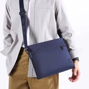 Men's navy blue oxford messenger bag with adjustable strap worn by model in white studio