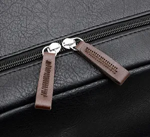 Detail showing smooth double metal zippers with brown leather pullers on a pebble grain bag