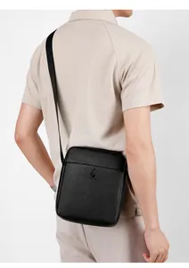 Close-up of black pebble leather crossbody bag with adjustable branded shoulder strap