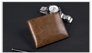 Close-up of brown leather bifold wallet with vintage texture, watch, and pen on dark desk