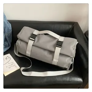 Detalle de la bolsa de viaje gris con correas blancas y hebilla en sofá de cuero