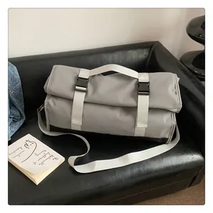 Bolsa de viaje gris con cierre enrollable y correas blancas sobre un sofá de cuero negro