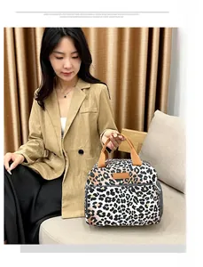 Détail d'un sac à lunch imprimé léopard avec poignées brunes porté par un modèle