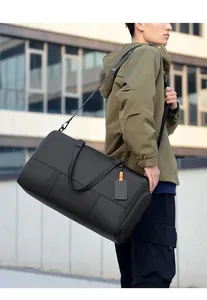 Male model wearing a matte black duffel bag with adjustable strap and luggage tag detail