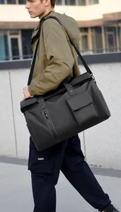 Man carrying a large black travel bag with adjustable strap in an outdoor setting
