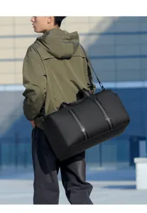 Detail of waterproof black travel duffel bag with reinforced straps worn by a model outdoors