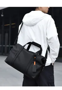 Man carrying a large black waterproof travel bag with reinforced handles and orange details