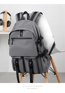 Deep gray multi-pocket backpack with buckles hanging on a white chair in a modern setting