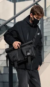 Outdoor urban view of a large black waterproof messenger bag with roll-top and buckles