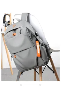 Detail of gray backpack with vibrant orange zippers and fashion tag on white chair