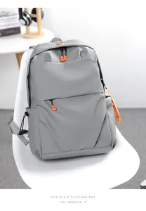 Grey waterproof nylon backpack with orange zippers on a white chair, close-up details