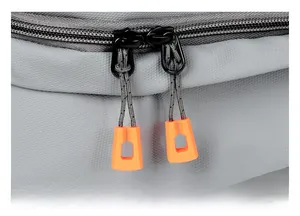 Close-up of dual black metal zippers with bright orange pull tabs on grey textured fabric
