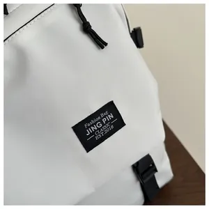 Detail of white nylon backpack featuring black woven label and zipper with cord pulls