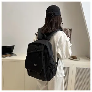 Rear view of model wearing a black nylon backpack with flap closure and brand label