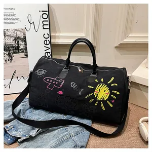 Detail of a large black canvas travel bag featuring colorful graffiti and a leather handle