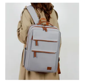 Rear view of model wearing a light gray commuter backpack with brown leather accents