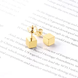 Minimalist polished gold titanium steel cube stud earrings for men on a vintage book page