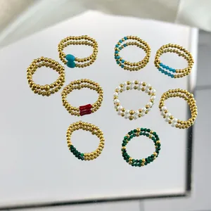 Set of 8 bohemian beaded rings with natural stones and gold beads on a reflective surface