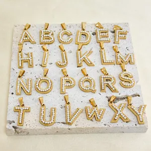 Macro view of 24 pearl-encrusted gold letter charms arranged on a textured stone surface