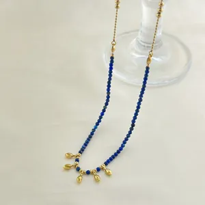 Lapis lazuli beaded necklace with gold teardrop pendants on an elegant glass holder