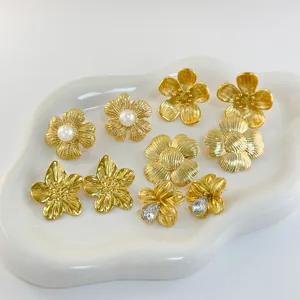Dettaglio di orecchini a fiore dorati con perle e cristalli su un vassoio di ceramica