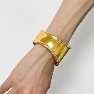 Polished 18K gold wave cuff bracelet worn on wrist showing glossy metallic texture