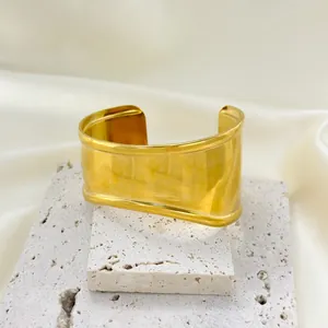 Detailed macro view of an 18K gold-plated wave cuff bracelet on a white stone display