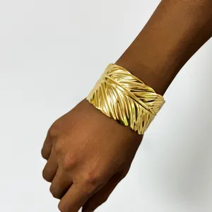 Close-up of wide golden feather bangle with detailed texture on model wrist