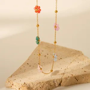 Detail of 18k gold plated chain necklace with colorful floral beads on stone texture