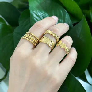 Set of four gold-plated rings with leaf, floral and coin patterns on hand with green leaves