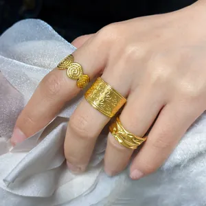 Drei goldene Edelstahlringe mit Spiral- und Reliefmustern auf weißer Seide