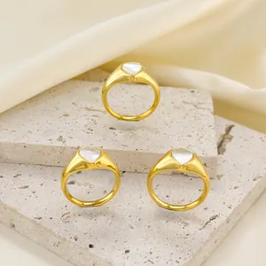Minimalist gold teardrop rings with white heart inlay on a stone pedestal