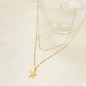 Double-layer gold necklace with white pearls and detailed starfish pendant on beige fabric
