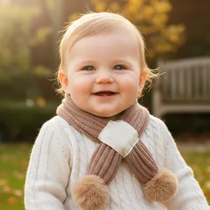 Close-up of knit baby scarf in brown with plush pom-poms and warm cross-over design