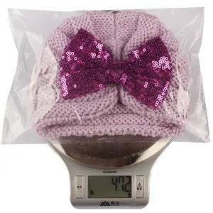 Détail du bonnet tricoté pour bébé pesant 47,2g avec un grand nœud à paillettes