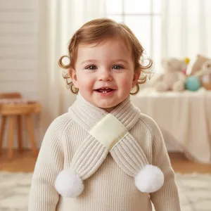 Detail of baby knitted cross scarf in cream with soft pom-poms for autumn winter