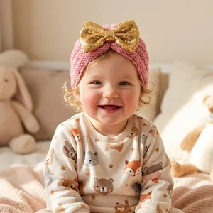 Gros plan sur un bandeau en tricot rose pour bébé avec un grand nœud doré à paillettes