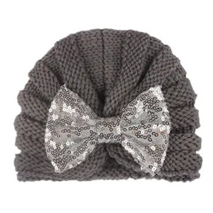 Détail du bonnet en tricot gris foncé pour bébé avec un grand nœud en paillettes argentées