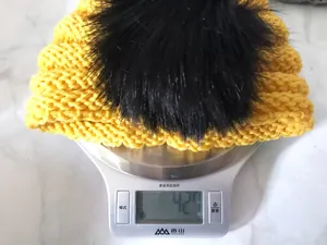 Dettaglio del cappello in maglia gialla per neonati con pompon che pesa 42,7g sulla bilancia