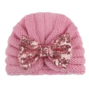 Détail du bonnet en tricot rose pour bébé avec un grand nœud en paillettes