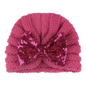 Détail d'un bonnet turban pour bébé en tricot rose avec un grand nœud en paillettes